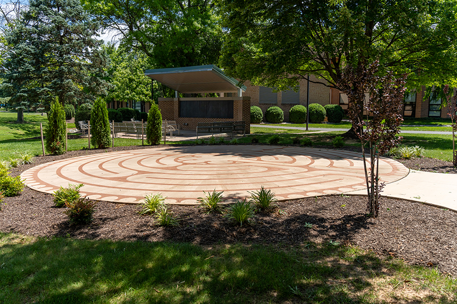 Outdoor circular labyrinth plaza with a winding brick pattern, surrounded by landscaped trees and benches.
